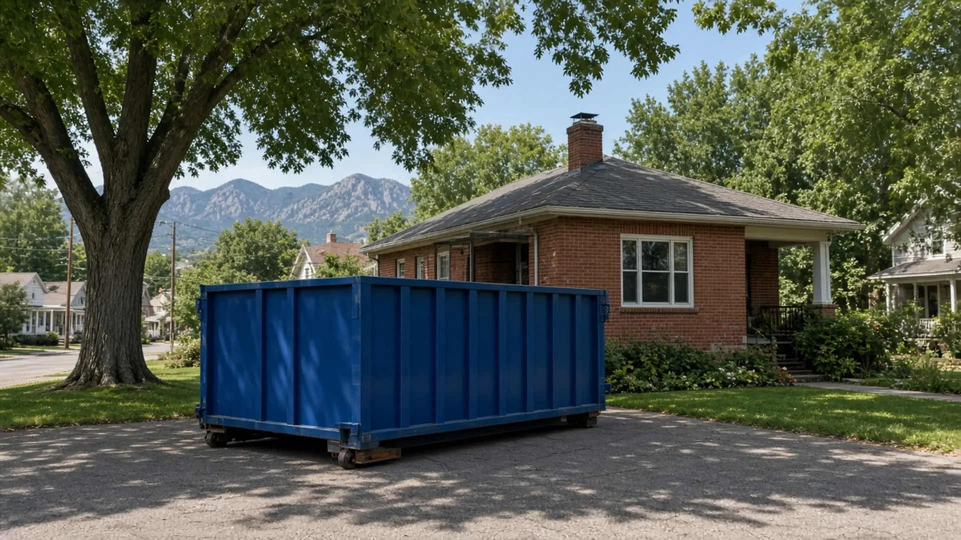 Blue roll-off dumpster on the driveway of a red-brick bungalow under mature trees in Louisville, Colorado